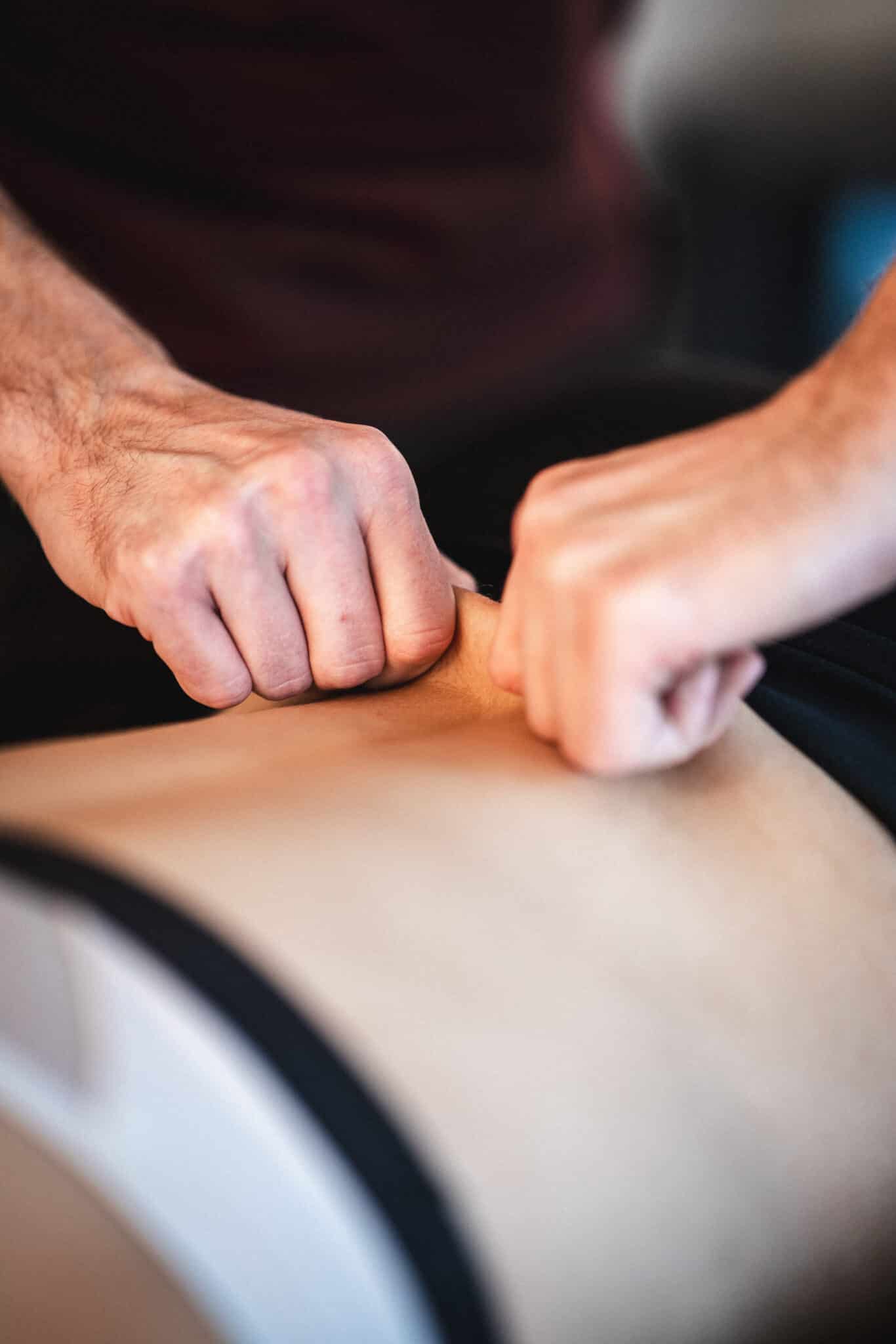 Nærbillede af terapeut der arbejder med muskelvæv for at løsne spændinger og mindske ømme muskler hos klienten.