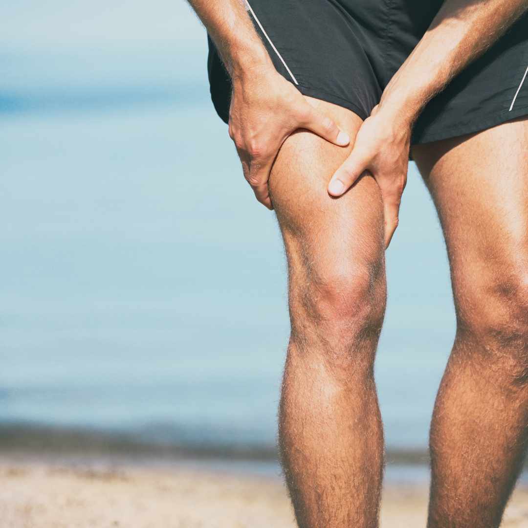 En mand står ved vandet og holder sig på låret med smerter efter træning som skyldes overbelastning og kan give ømme muskler.