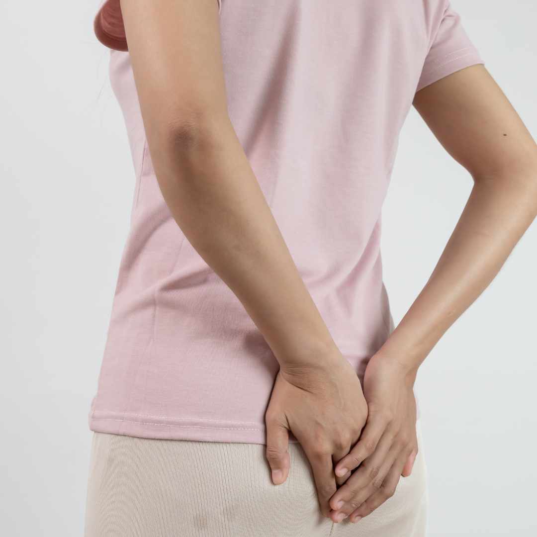 Person holder sig på halebenet på grund af halebenssmerter ved siddestilling.