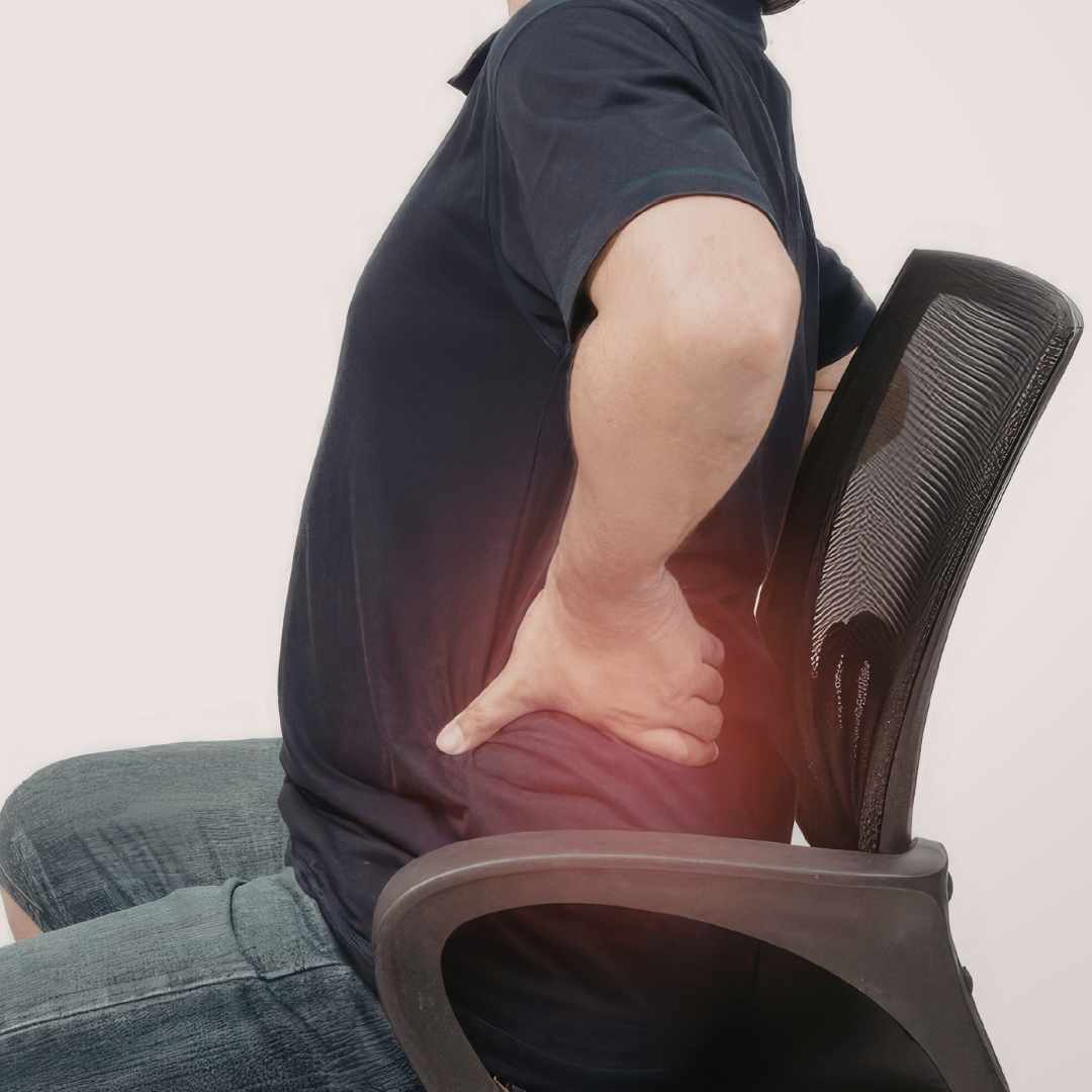 Mand sidder på kontorstol og holder sig på lænden ved lændesmerter og spændinger i ryggen.
