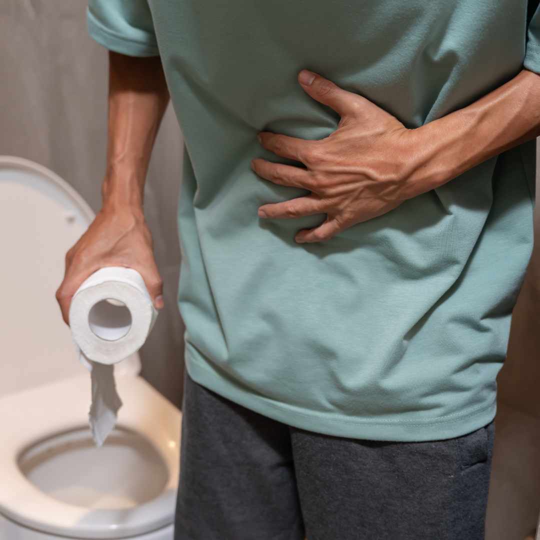 Mand med diarré og mavesmerter står ved toilettet og holder sig på maven på grund af ubehag.